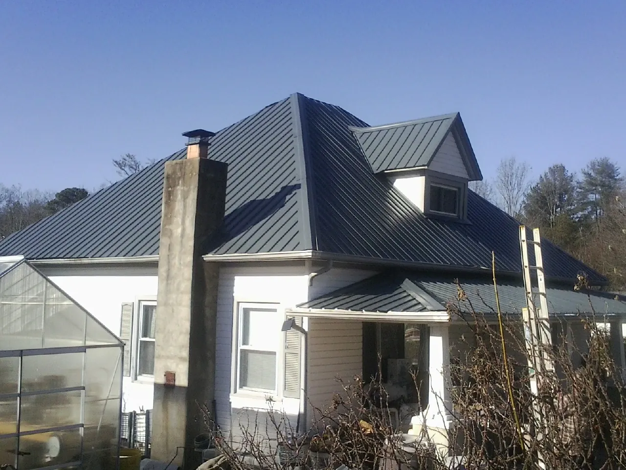 Dark blue standing seam metal roof on a white farmhouse with dormer — Slate & Tile Roof Repair by Roofing Brothers in Shoreham