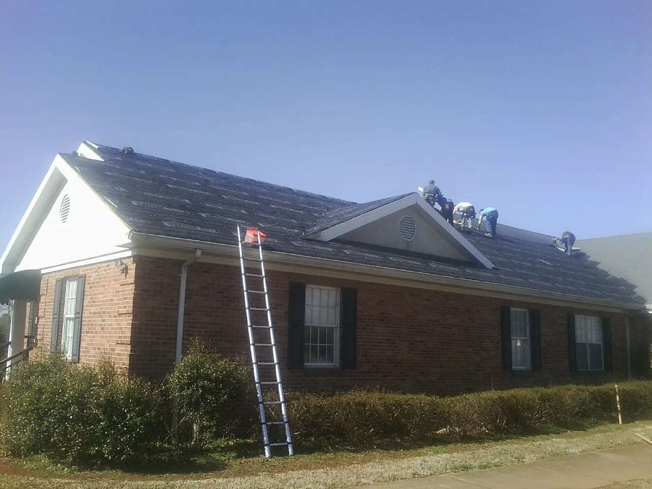 Crew tearing shingles off a brick ranch roof with a ladder set — Emergency Roof Repair work by our crew in Shoreham