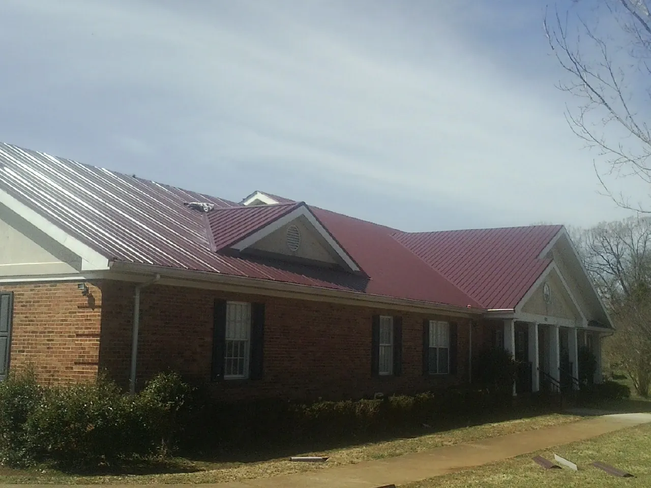 Red metal roof with gabled entries on a long brick building, from a Hail Damage Roof Repair job in Shoreham