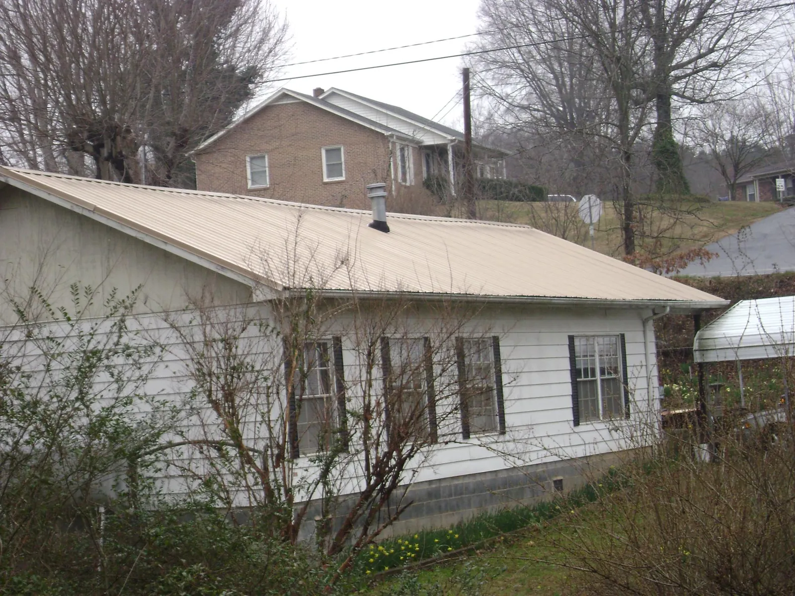 Tan metal roof on a white sided house set into a hillside — Commercial Roofing by Roofing Brothers in Shoreham